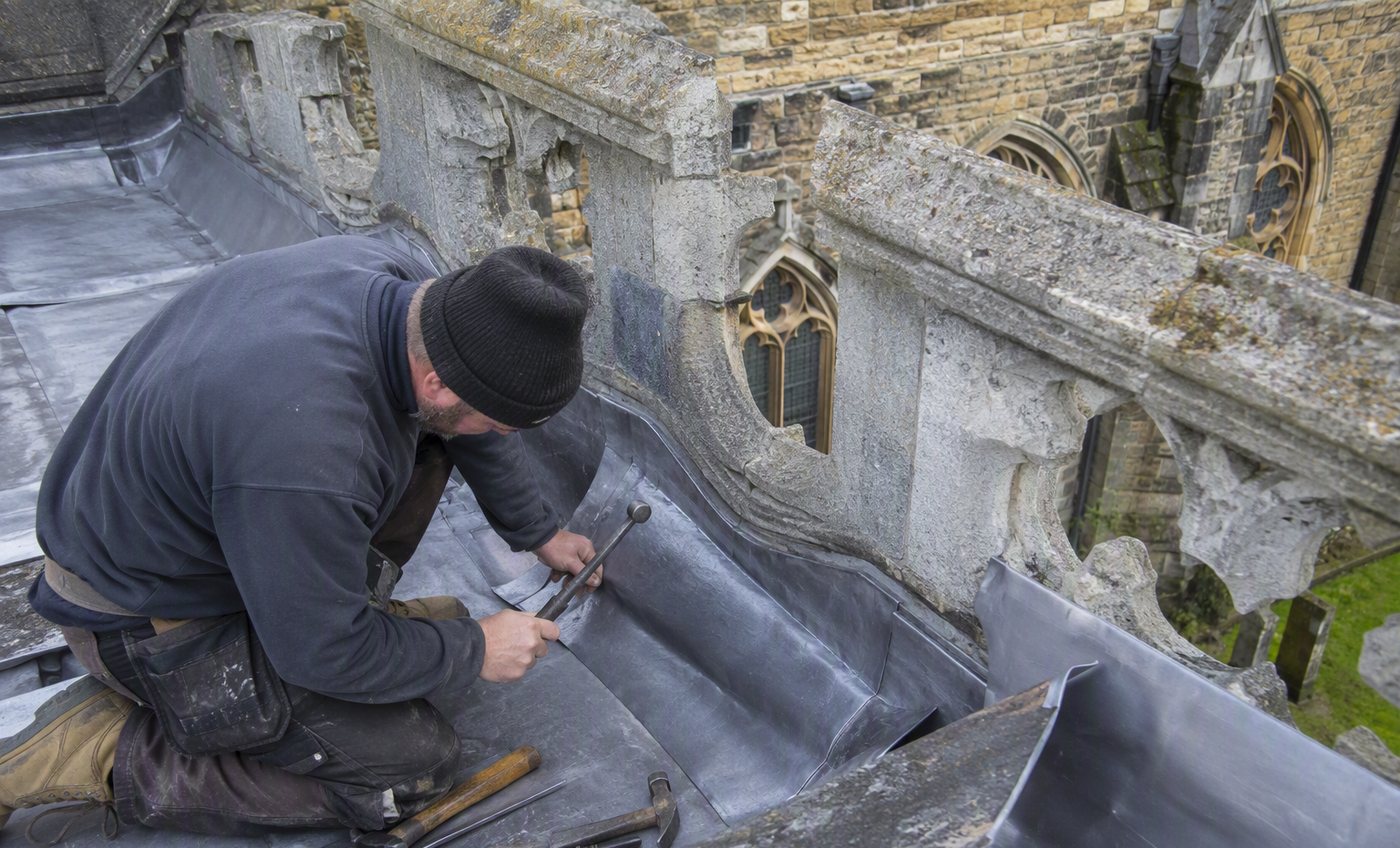 Roofer dressing new lead flashing around a chimney stack